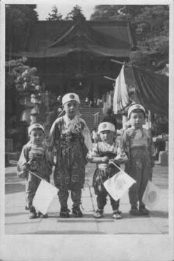 写真12　山門の前で。祭装束を着た子どもたちだが、頭には日の丸の鉢巻き、手には国旗の戦勝祈願スタイル。